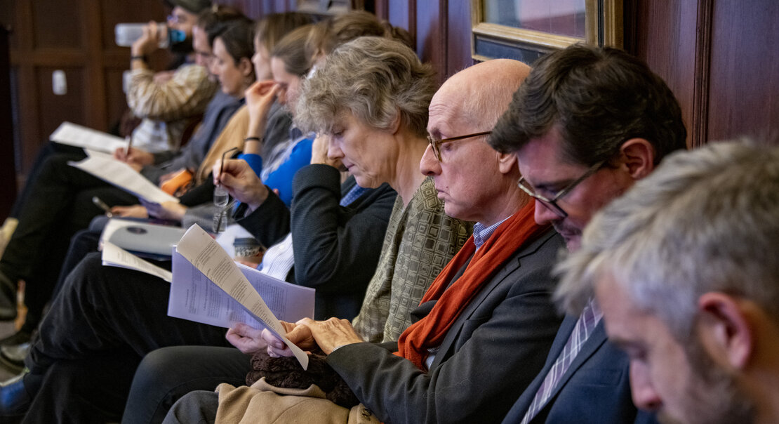 several people sitting along a wall reading research papers